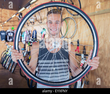 Portrait of smiling young man holding roue de bicyclette en magasin de bicyclettes Banque D'Images