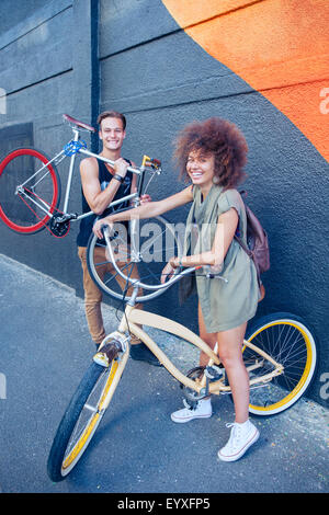 Portrait smiling friends avec des vélos à côté du mur urbain Banque D'Images