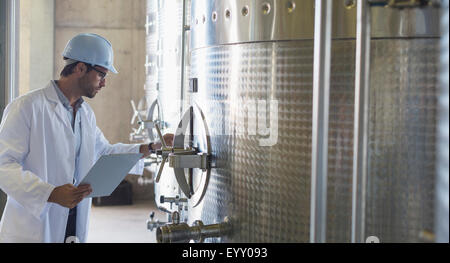 Vigneron in lab coat and hard hat l'examen de la tva en acier inoxydable en cave Banque D'Images Vigneron in lab coat and hard hat l'examen de la tva en acier inoxydable en cave Banque D'Images