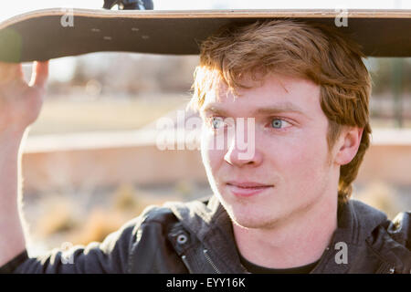 Caucasian teenage boy holding skateboard en plein air Banque D'Images