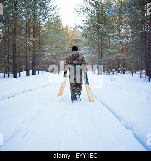 Caucasian man carrying skis sur route enneigée Banque D'Images