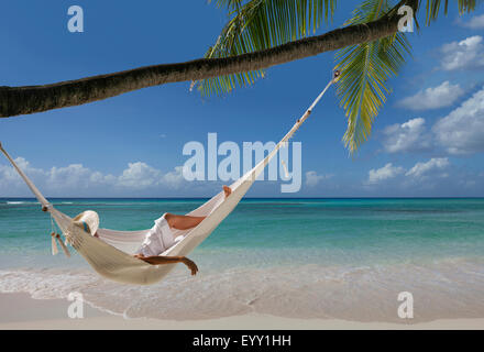 Caucasian woman laying in hammock sous palm tree on tropical beach Banque D'Images