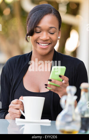 Mixed Race businesswoman using cell phone at outdoor cafe Banque D'Images