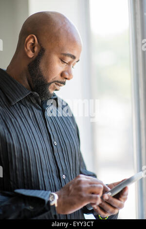 Black man using cell phone near window Banque D'Images