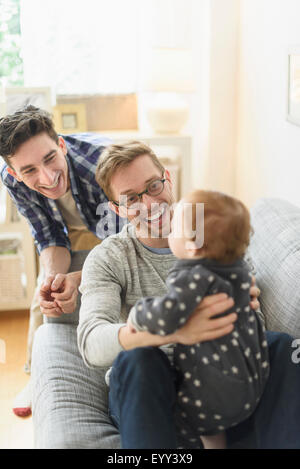 Caucasian gay fathers and baby relaxing on sofa Banque D'Images