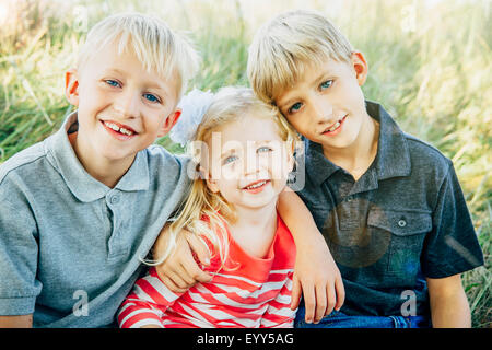 Caucasian brothers and sister smiling in grass