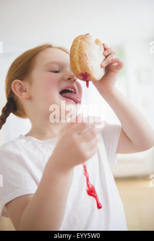 Caucasian girl licking messy jelly donut Banque D'Images