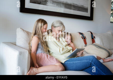 Grand-mère de race blanche et petites-filles using digital tablet on sofa Banque D'Images