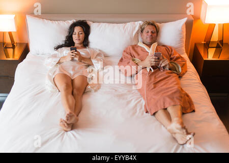 L'utilisation de téléphones cellulaires couple on bed Banque D'Images