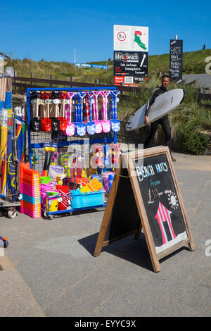 Boutique vendant des jouets de plage, des seaux et des pelles avec surfer walking passé, Bude, Cornwall, England, UK Banque D'Images