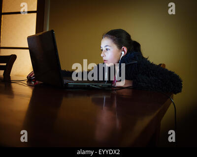 Mixed Race girl using laptop at table de nuit Banque D'Images