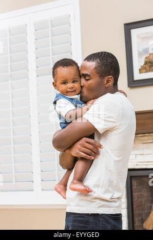 Black father kissing baby son in living room Banque D'Images