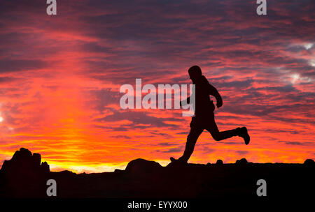 Un homme court sur éboulis rouge au coucher du soleil, Lake District, UK Banque D'Images