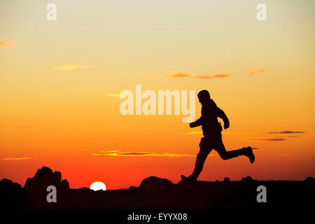 Un homme court sur éboulis rouge au coucher du soleil, Lake District, UK Banque D'Images