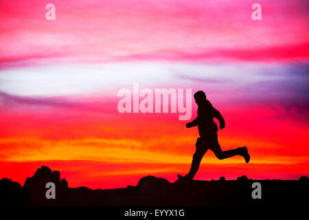 Un homme court sur éboulis rouge au coucher du soleil, Lake District, UK Banque D'Images