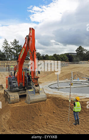 Un géomètre est titulaire d'un pôle allant en face d'un grand sur une pelle sinon déserté construction site Banque D'Images