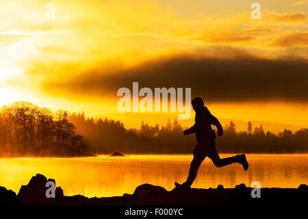 Le lever du soleil sur le lac Windermere à Ambleside, Lake District, UK, avec un homme qui court passé. Banque D'Images