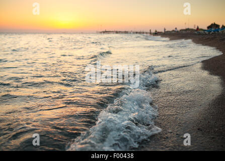 La mer brillante vagues sur la plage de sable dans la lumière au coucher du soleil Banque D'Images