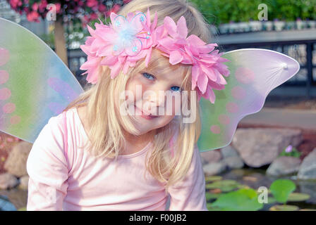 Smiling little girl wearing a laurel rose fleurs dans les cheveux et des ailes de fées. Banque D'Images