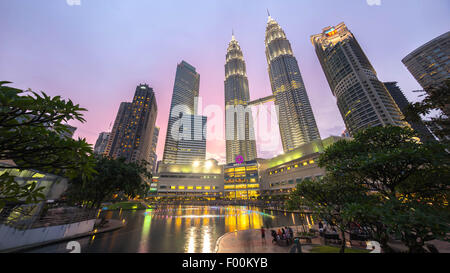 Fontaine à eau avec Suria KLCC Petronas Towers et les immeubles de bureaux à l'heure bleu coucher du soleil dans la nuit. Banque D'Images