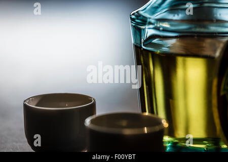 Une bouteille de boisson alcoolisée japonaise le souci et en céramique tasses de saké dans le rétro-éclairage sur une table en bois sombre. Banque D'Images