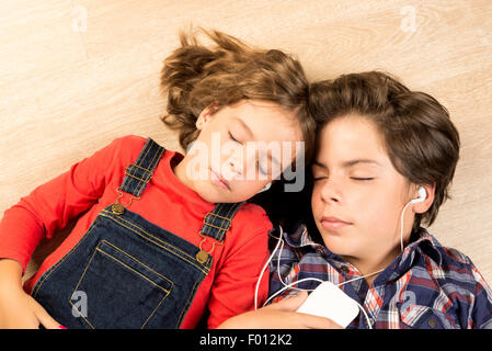Portrait des enfants d'écouter de la musique avec des écouteurs, tendue sur un parquet à la maison Banque D'Images