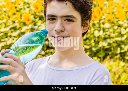 Salon de l'environnement - Caucasian boy dans un champ de tournesols est sur le point de boire de l'eau claire d'une bouteille en plastique bleu vert d'étancher sa soif par une chaude journée d'été et lumineux Banque D'Images