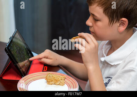 Jeune garçon à l'aide de l'iPad tout en mangeant le petit déjeuner. M. Banque D'Images