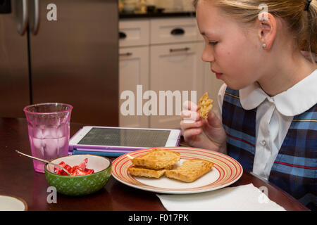 Jeune fille (11 ans) La lecture sur son iPad en mangeant le petit déjeuner. M. Banque D'Images