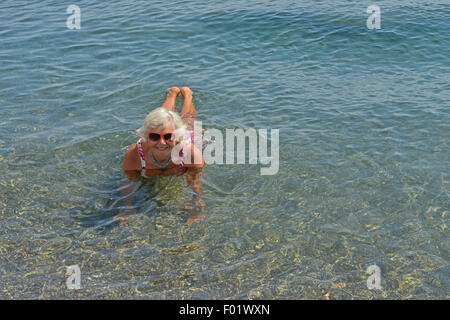 Portrait de senior lady c'est couché dans l'eau peu profonde de la mer de galets de plage. Banque D'Images