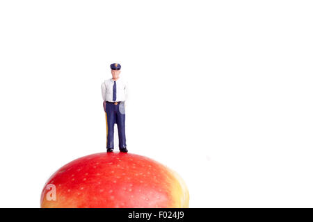 Petite figure d'un policier debout sur une pomme, isolated on white Banque D'Images
