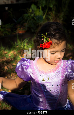 Cinq ans fille avec une fleur de géranium rouge sur la tête. Banque D'Images