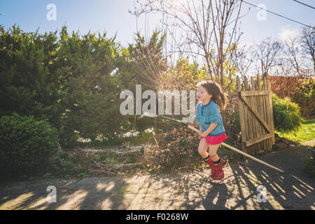 Young Girl riding râteau dans yard comme c'est un cheval Banque D'Images