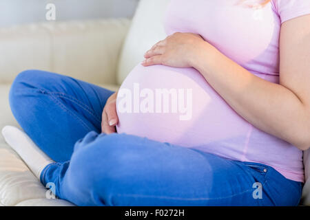 Close up of pregnant woman sitting on couch milk Banque D'Images