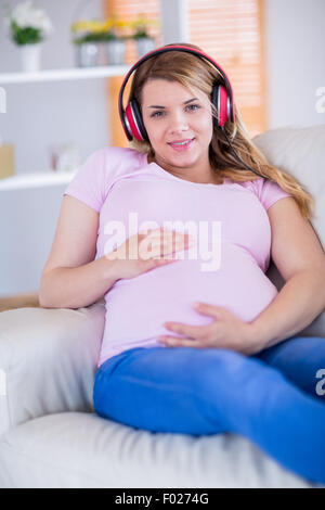 Smiling pregnant woman listening music et de toucher son ventre Banque D'Images