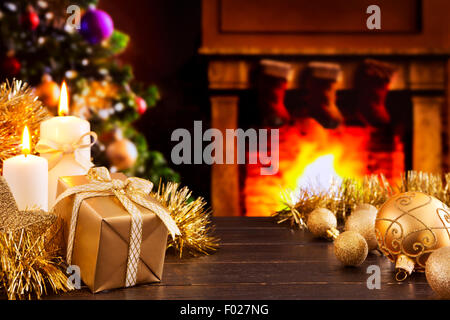 Décorations de Noël, un cadeau et des bougies devant une cheminée. Un feu brûle dans la cheminée. Banque D'Images