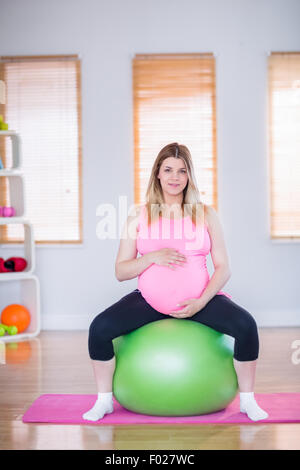 Pregnant woman looking at camera sitting on exercise ball Banque D'Images