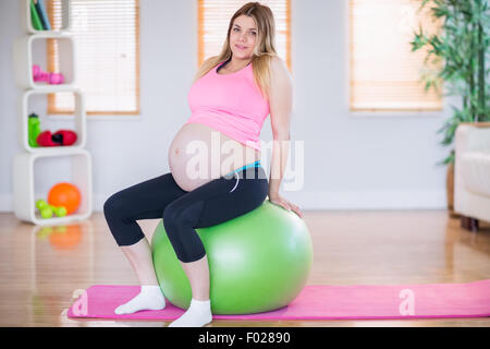 Pregnant woman looking at camera sitting on exercise ball Banque D'Images