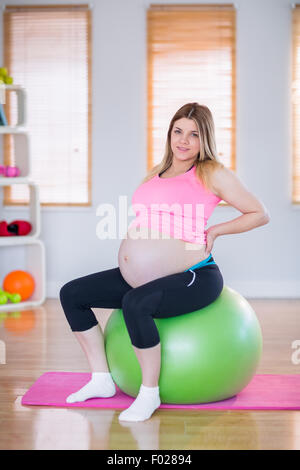 Pregnant woman looking at camera sitting on exercise ball Banque D'Images