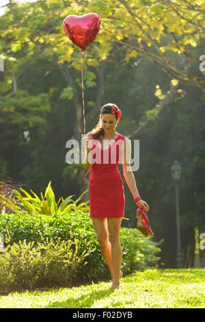 Woman walking in park holding heart shaped balloon, l'exécution shoes Banque D'Images