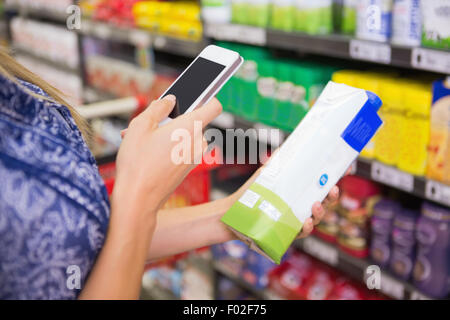 Femme comparaison du prix d'un carton de lait avec son téléphone Banque D'Images