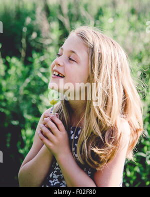 Portrait of a smiling girl holding a buttercup sous son menton Banque D'Images
