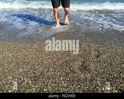 La section basse d'un homme marchant dans le surf Banque D'Images