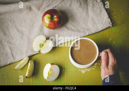 Main humaine tenant une tasse de café et couper les pommes sur la table Banque D'Images