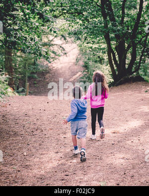 Vue arrière de deux enfants qui courent dans les bois Banque D'Images