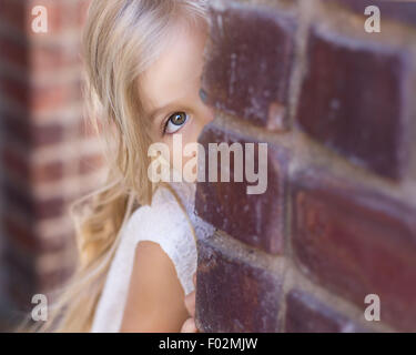 Girl peeking autour d'un mur de briques Banque D'Images