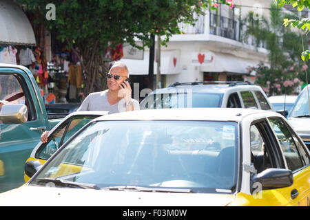 L'homme à Puerto Vallarta, au Mexique, il est en conversation sur son téléphone en entrant dans un taxi. Homme, 55 ans, hispaniques ethnicit Banque D'Images