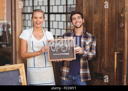 Smiling waitress and man holding chalkboard with open sign Banque D'Images