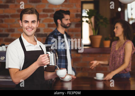 Smiling barista pouring lait en cup face aux clients Banque D'Images