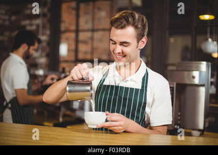 Smiling barista de verser le lait dans une tasse Banque D'Images